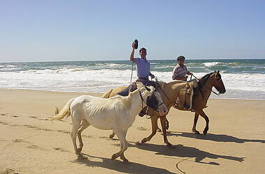 Gauchos reiten am Strand und führen ein weißes Pferd