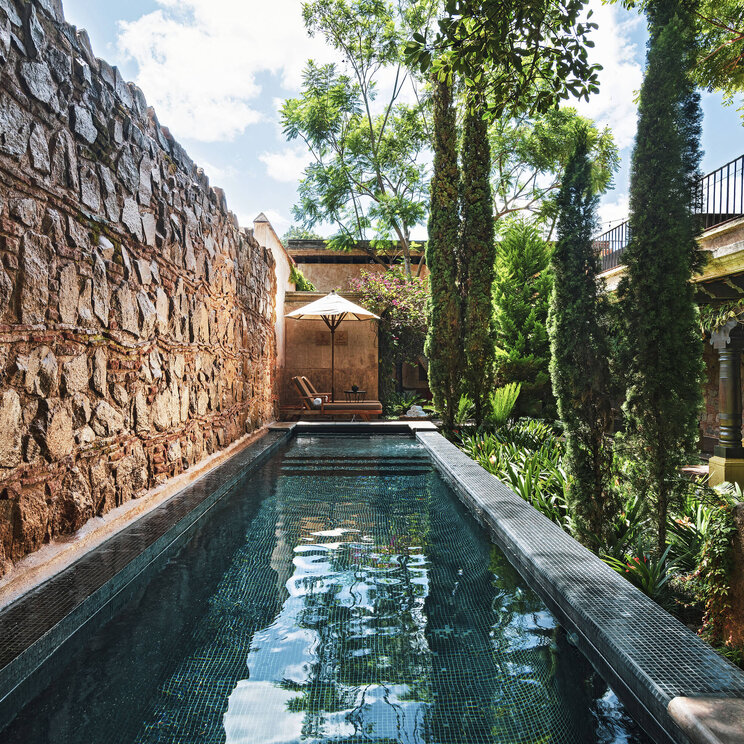 Pool im Innenhof des El Convento Boutique Hotels in Antigua, Guatemala, umgeben von Natursteinmauern, Zypressen und kolonialer Architektur.