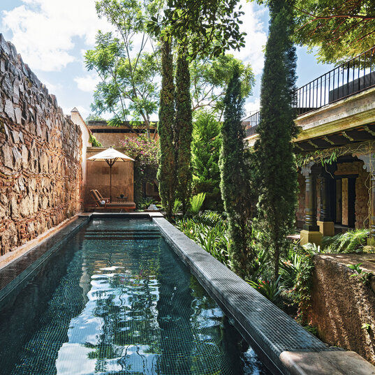 Pool im Innenhof des El Convento Boutique Hotels in Antigua, Guatemala, umgeben von Natursteinmauern, Zypressen und kolonialer Architektur.