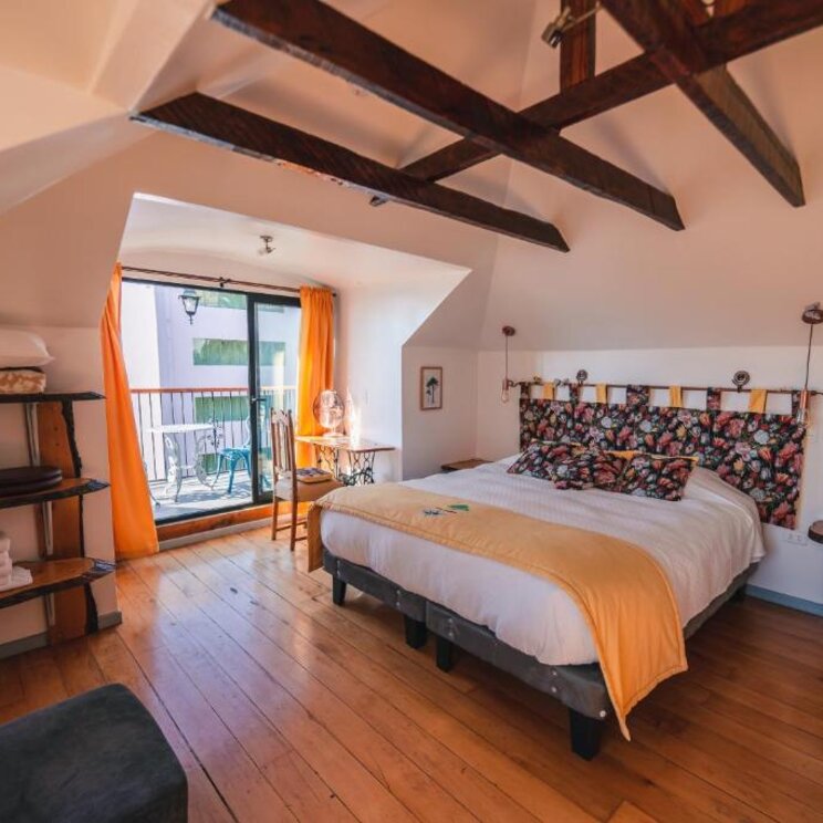Schlafzimmer im Dachgeschoss mit Holzbalken, Doppelbett und Balkonzugang in Valparaiso.