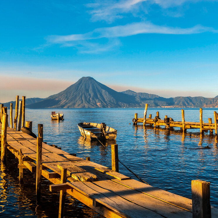 Holzstege und Boote am Lago Atitlán in Guatemala mit Blick auf den imposanten Vulkan im warmen Licht der Abendsonne.