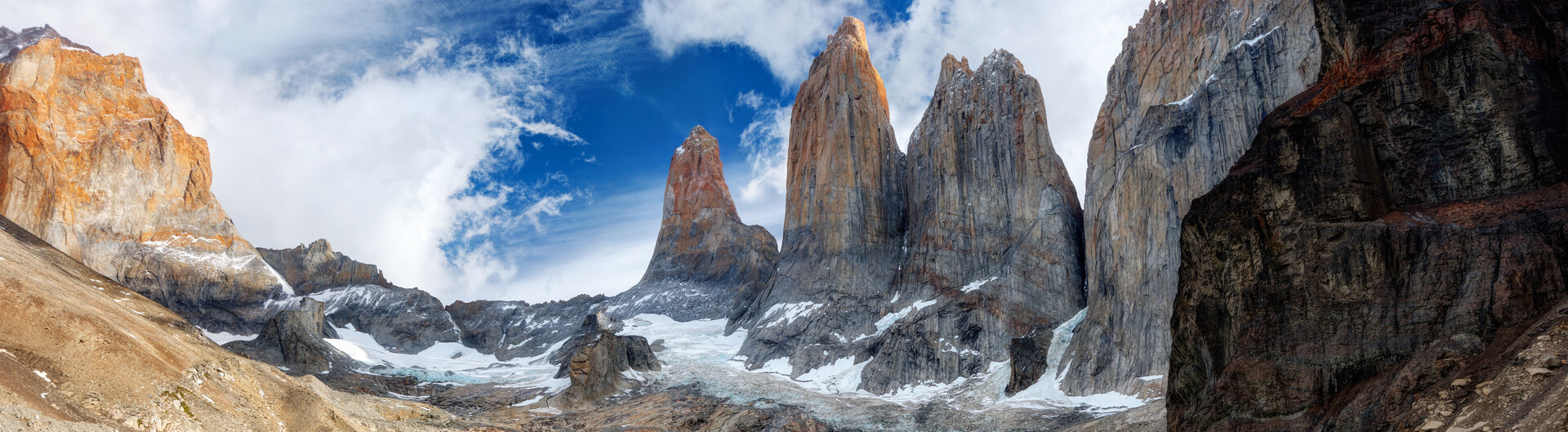 Drei Granittürme Torres del Paine in Chile über einem türkisfarbenen Gletschersee unter blauem Wolkenhimmel.