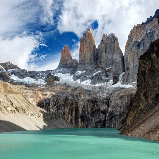 Drei Granittürme Torres del Paine in Chile über einem türkisfarbenen Gletschersee unter blauem Wolkenhimmel.