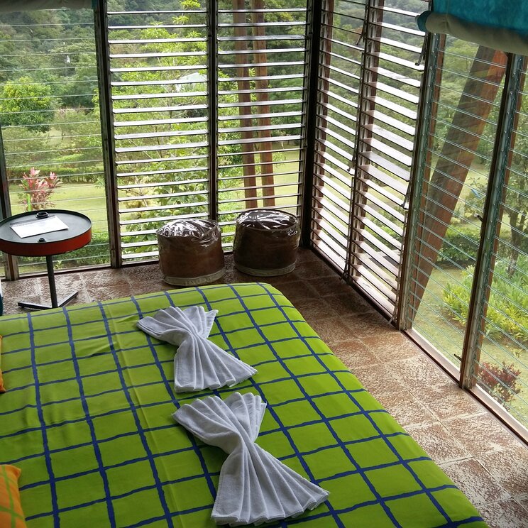 Standardzimmer der Celeste Mountain Lodge in Costa Rica mit buntem Bett und grossen Lamellenfenstern zum Garten.