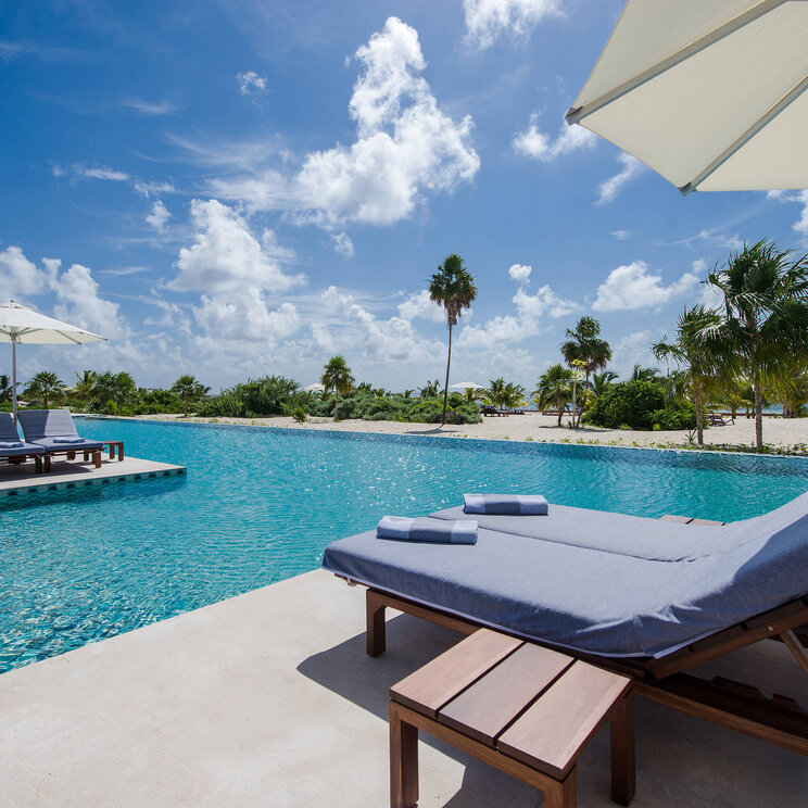 Poolbereich im Hotel Chablé Maroma in Punta Maroma, Quintana Roo, Mexiko, mit komfortablen Liegen, Sonnenschirmen und Blick auf Palmen und den weißen Sandstrand.