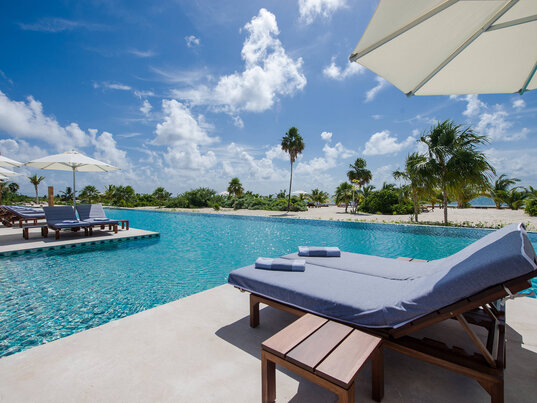 Poolbereich im Hotel Chablé Maroma in Punta Maroma, Quintana Roo, Mexiko, mit komfortablen Liegen, Sonnenschirmen und Blick auf Palmen und den weißen Sandstrand.