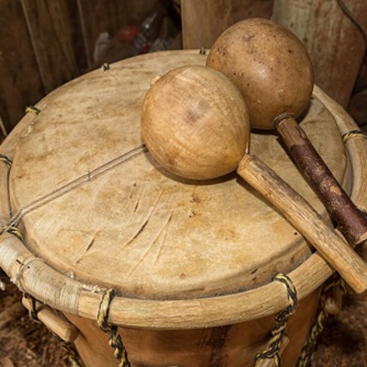Handgefertigte Trommel mit zwei Kalebassen-Rasseln auf einem Holzboden in Belize, traditionell verwendet in der Musik der Garifuna-Kultur.