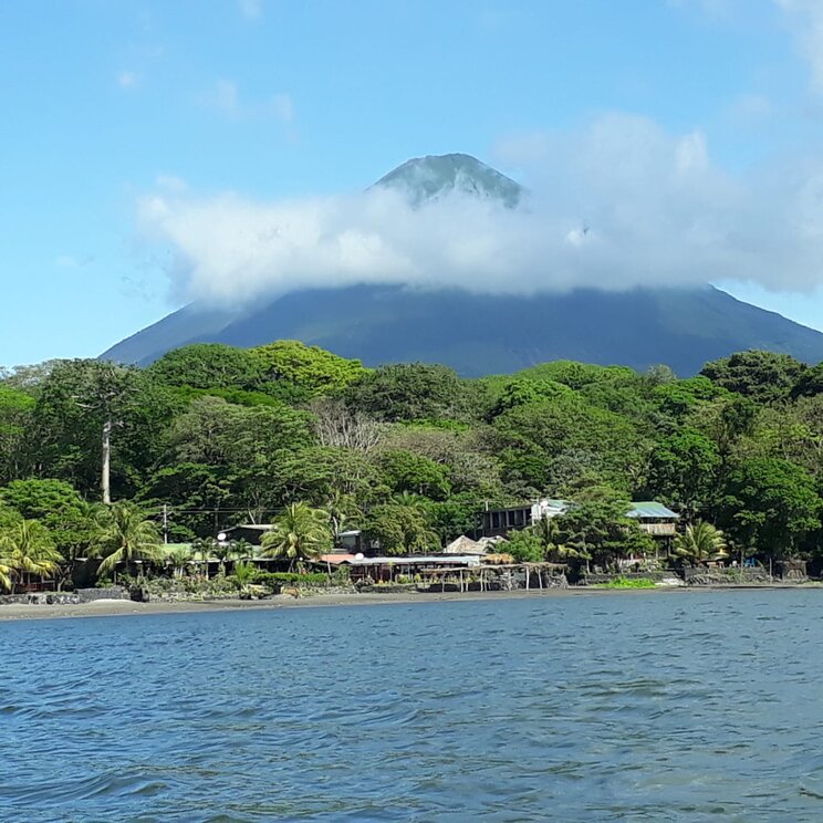 Blick vom Nicaraguasee auf das Hotel Villa Paraíso auf der Insel Ometepe, Nicaragua, mit tropischer Vegetation und dem Vulkan Concepción im Hintergrund.