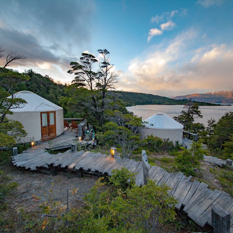 Verschlungene Holzstege führen zwischen Bäumen zu weißen Jurten am Ufer des Lago Toro, Patagonia Camp, Chile.