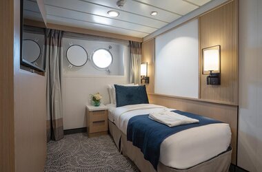 Komfortable Einzelkabine auf der Ocean Albatros mit Bullaugen, gemütlichem Bett und moderner Ausstattung für Alleinreisende.