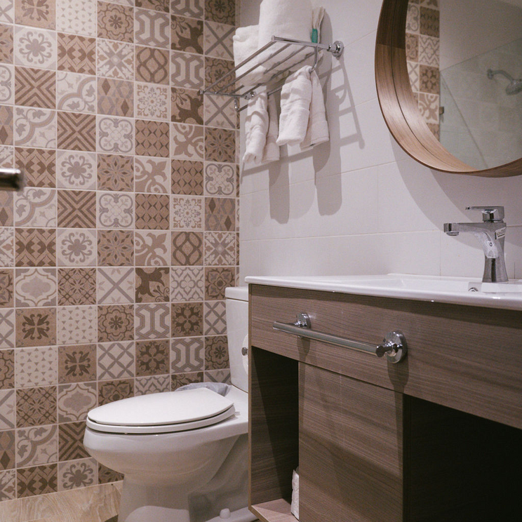 Modernes Badezimmer im Hotel Pinar Dorado in Jarabacoa, Dominikanische Republik, mit gemusterten Fliesen, rundem Spiegel und heller Holzausstattung.