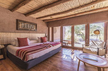 Schlafzimmer mit Doppelbett, Holzdecke und Terrassenzugang im Hotel Cumbres San Pedro, Chile.
