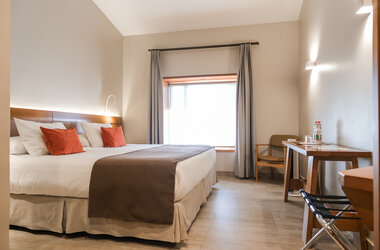 Doppelzimmer mit hellen Waenden, Holzschreibtisch und Fenster unter einer Dachschraege in der Atacama-Wüste.