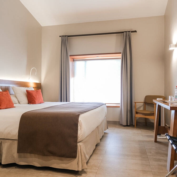 Doppelzimmer mit hellen Waenden, Holzschreibtisch und Fenster unter einer Dachschraege in der Atacama-Wüste.