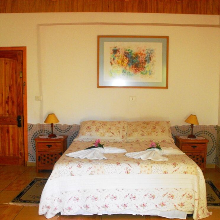 Doppelbett mit geblümter Bettwaesche, Nachttischen und bunter Grafik an der Wand in einem Hotelzimmer auf der Osterinsel.