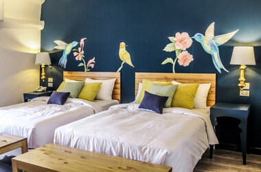 Zwei Betten vor einer dunkelblauen Wand mit Wandmalereien von Kolibris und Blumen im Hotel Tariq in Cusco.