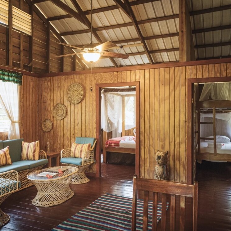 Wohnbereich im Farmhaus mit blauen Sofas, Korbsesseln und Holzwänden in San Ignacio, Belize.