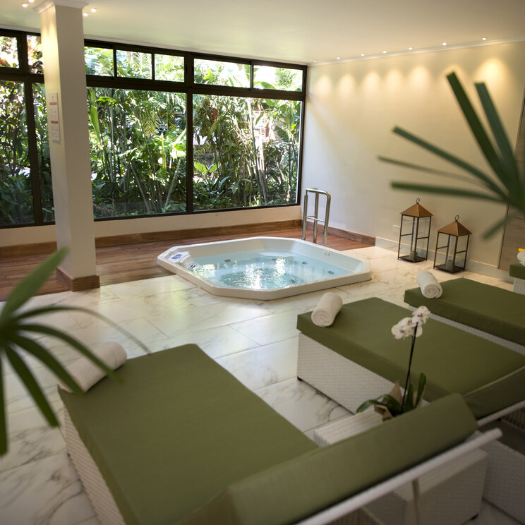 Indoor-Wellnessbereich in Lateinamerika mit Whirlpools, Liegen und Blick auf tropische Pflanzen.