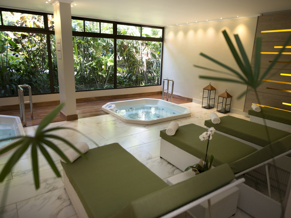 Indoor-Wellnessbereich in Lateinamerika mit Whirlpools, Liegen und Blick auf tropische Pflanzen.