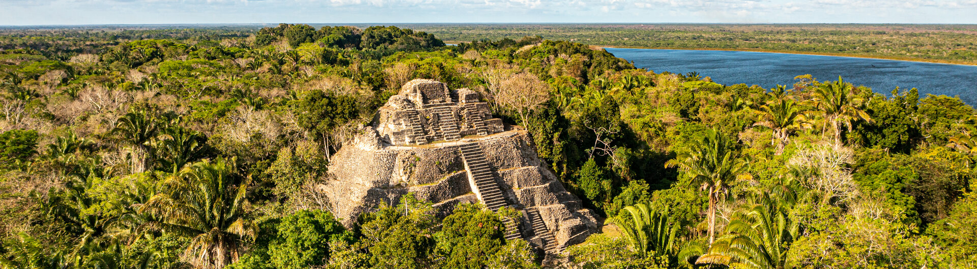 Hohe Maya-Pyramide von Lamanai umgeben von dichtem Dschungel an einem Fluss in Belize.