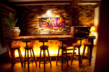 Hotelbar mit beleuchteter Front, hohen Barhockern, Holzelementen und buntem Wandbild in Peru.