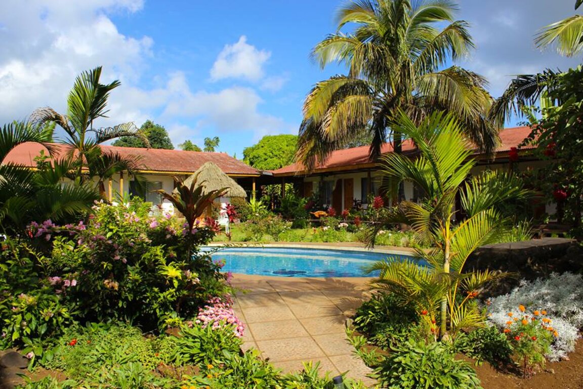 Tropische Gartenanlage mit Swimmingpool, Palmen und blühenden Strauchpflanzen vor den Hotelgebaeuden des Hotel Gomero.