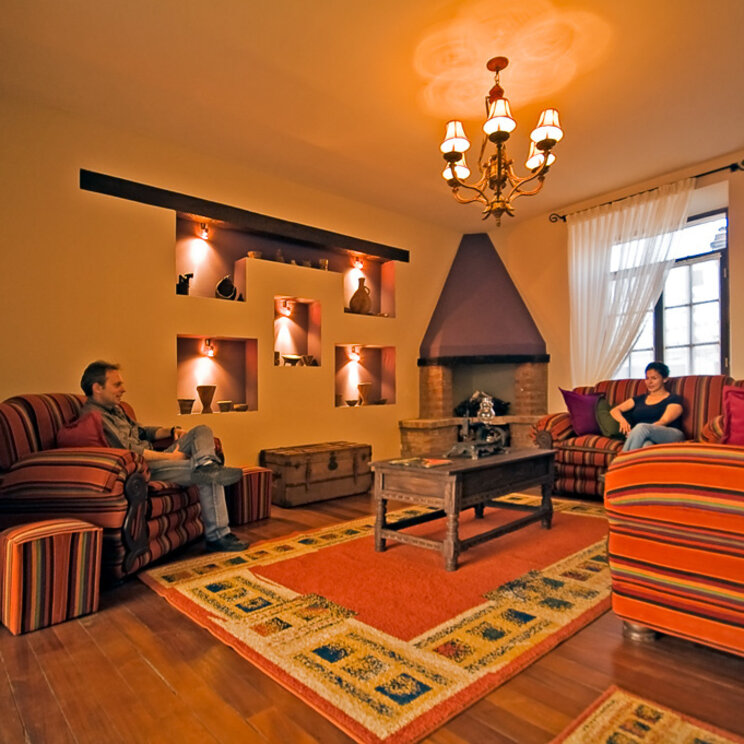 Hotellobby in Sucre mit gestreiften Sesseln, Kamin und beleuchteten Wandnischen mit Tongefaessen.