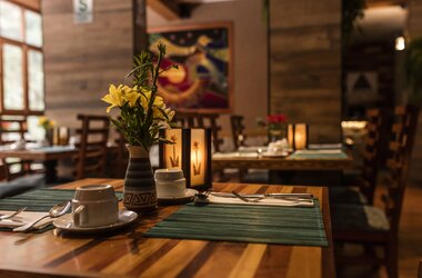 Gedeckter Holztisch mit gelben Blumen, Kerzenleuchter und Kaffeetasse im Restaurant in Aguas Calientes.