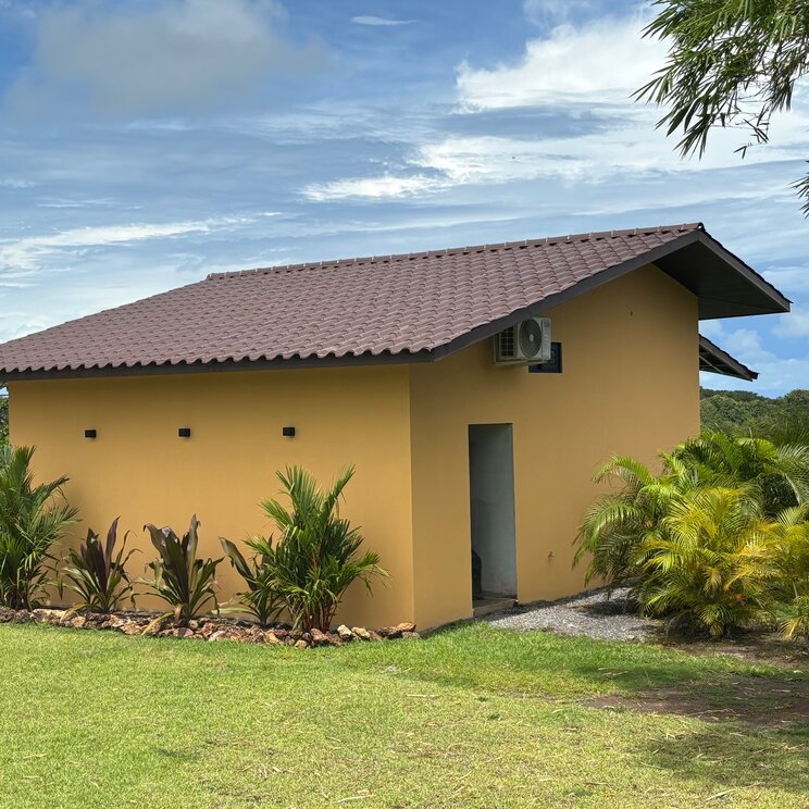 Gelber Bungalow mit Ziegeldach vor tropischer Vegetation und bewölktem Himmel in Boca Chica.