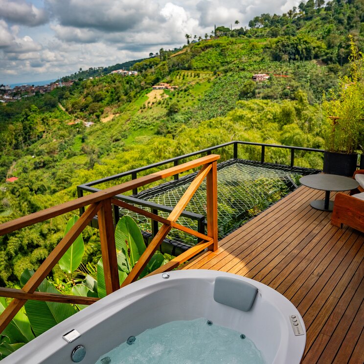 Whirlpool auf Holzterrasse mit Blick auf gruene Huegelketten in Kolumbien.