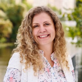 Giselle Beyer Thó, Mitarbeiterin bei Gateway Lateinamerika, steht lächelnd auf einer Brücke mit grünem Flussufer im Hintergrund.