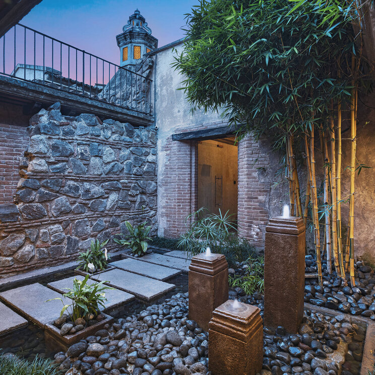 Stimmungsvoll beleuchteter Innenhof im El Convento Boutique Hotel in Antigua, Guatemala, mit Natursteinmauern, Bambus, Wasserbecken und kolonialem Flair – ruhige Oase im historischen Zentrum.