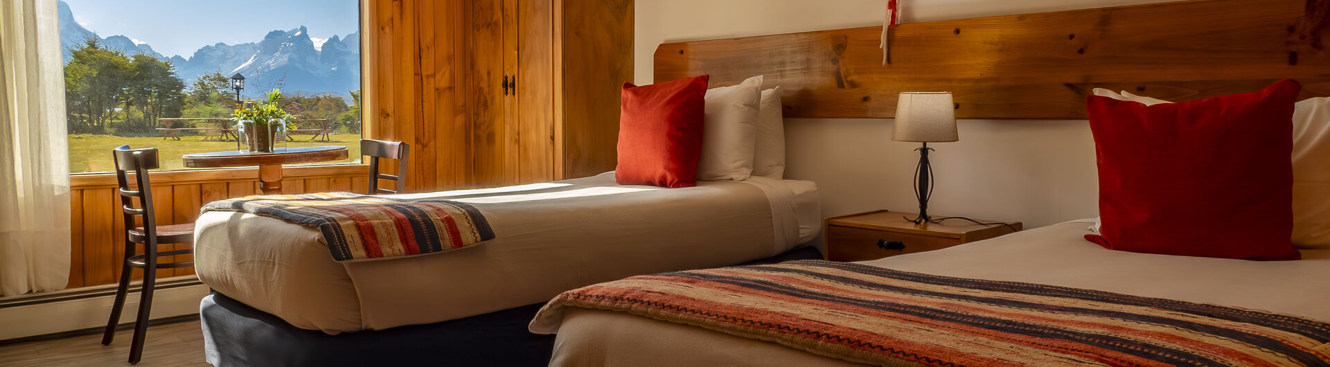 Zweibettzimmer im Hotel del Paine mit Holzverkleidung, roter Dekoration und Panoramafenster mit Bergblick im Nationalpark Torres del Paine, Chile.