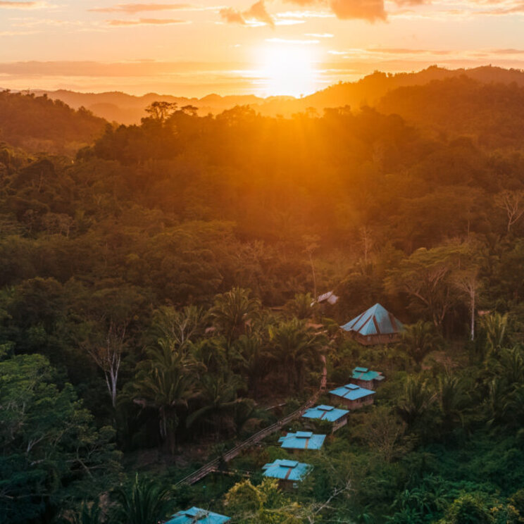 Luftaufnahme des Regenwalds mit kleinen Häusern bei Sonnenuntergang in San Ignacio, Belize.