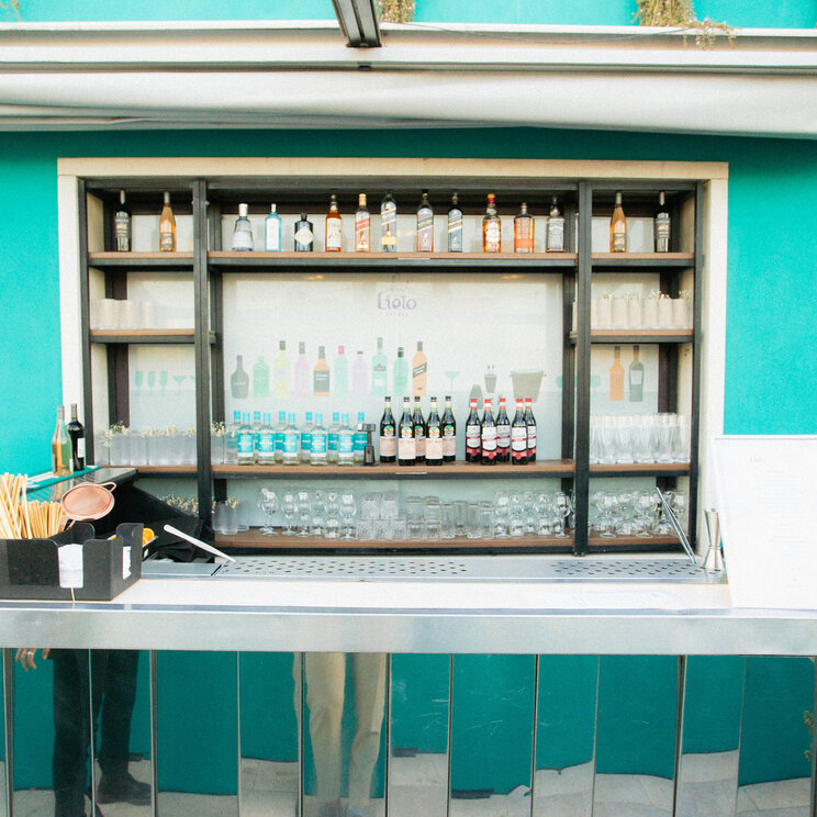 Rooftop-Bar mit verspiegelter Front, Flaschenregal und Glaesern vor einer tuerkisfarbenen Wand in Buenos Aires.