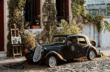 Schwarzer Oldtimer steht auf Kopfsteinpflaster vor einem pflanzenbewachsenen Haus in Uruguay