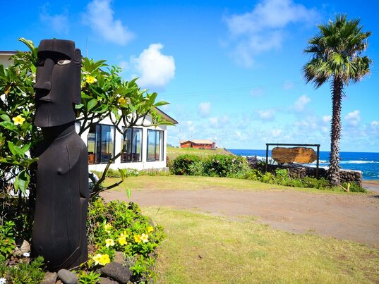 Außenbereich des Hotel Taha Tai auf der Osterinsel mit Moai-Statue, Palmen und Blick auf den Pazifik.
