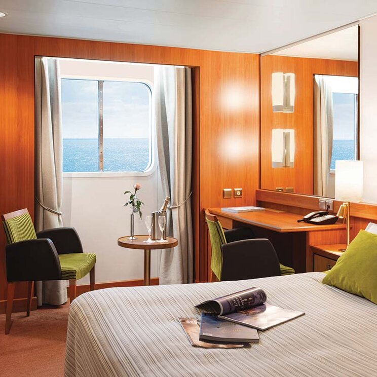 Außenkabine auf der Ocean Seaventure Antarktis Expeditionskreuzfahrt mit Doppelbett, Sitzecke, Schreibtisch und Bullauge mit Meerblick.