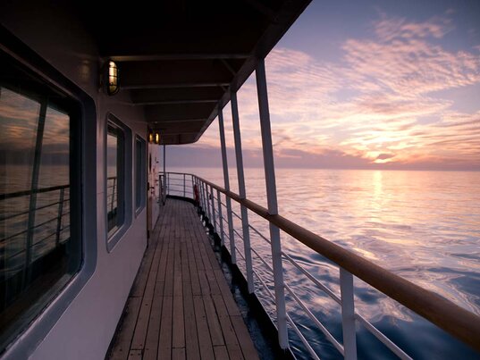 Außendeck der Ocean Seaventure Antarktis Expeditionskreuzfahrt mit Holzplanken, Reling und Blick auf das Meer bei Sonnenuntergang.