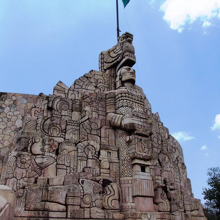 Monumento a la Patria in Mérida, Mexiko, mit detaillierten Steinreliefs und der mexikanischen Flagge an der Spitze.