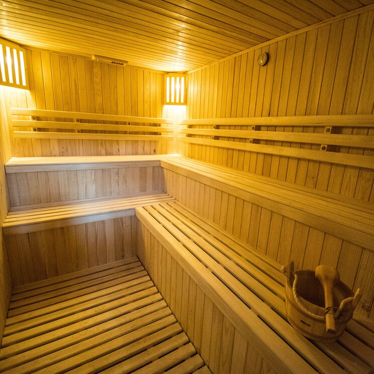 Innenansicht einer hölzernen Sauna im Hotel Rio Serrano mit mehrstufigen Sitzbänken und einem hölzernen Aufgusseimer.