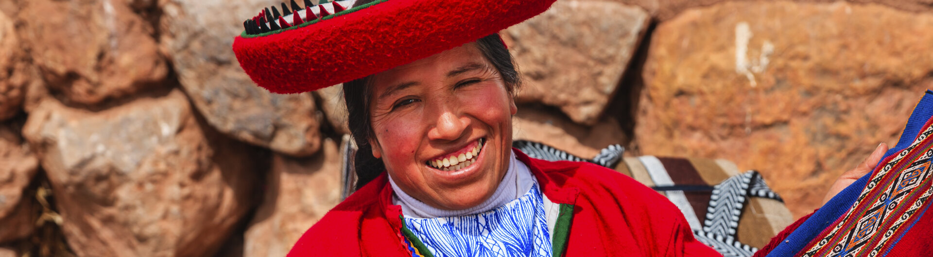 Lachende Frau aus Peru in roter Tracht mit einem roten Webtuch. 