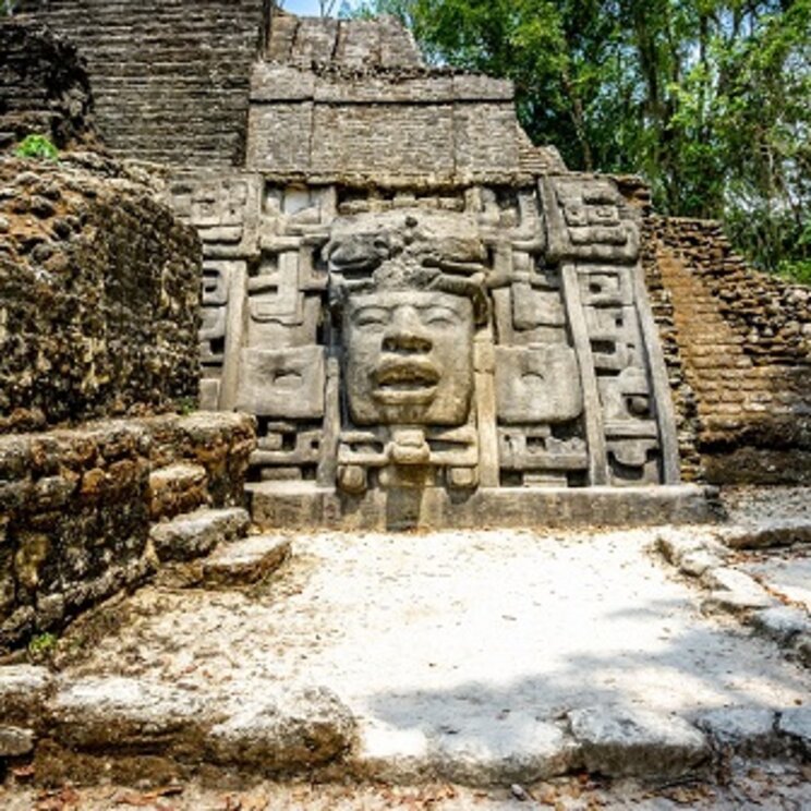 Gut erhaltenes Tempelrelief in der Maya-Stätte Lamanai im Dschungel von Belize mit monumentalem Gesicht und umgebenden Steinstrukturen.
