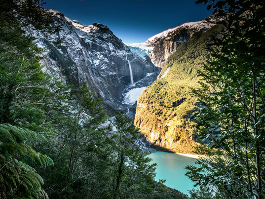 Hängender Gletscher Ventisquero Queulat mit Wasserfall über einer türkisfarbenen Lagune in Chile, gerahmt von Regenwald.