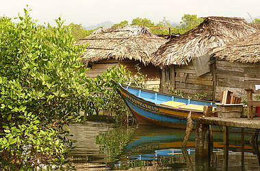 Boot am Steg vor palmenbedeckten Hütten