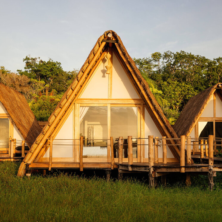 Bungalows im Hotel Our Habitas Bacalar in Mexiko mit A-förmiger Architektur, großen Glasfronten und Blick ins Grüne.