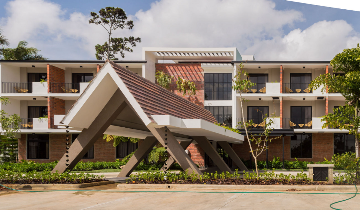 Außenansicht des Hotel Pinar Dorado in Jarabacoa, Dominikanische Republik, mit moderner Architektur, markantem Eingangsbereich und Balkonzimmern mit Hängematten.