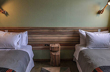 Zimmer mit Twinbetten, Teppich mit buntem, geometrischem Muster und Holzdekoration im Hotel Vendaval