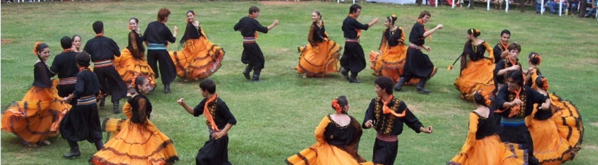 Festival in Paraguay mit traditionellen Tänzern in auffälligen orangefarbenen und schwarzen Kostümen, die auf einer offenen Wiese vor einem Publikum auftreten.