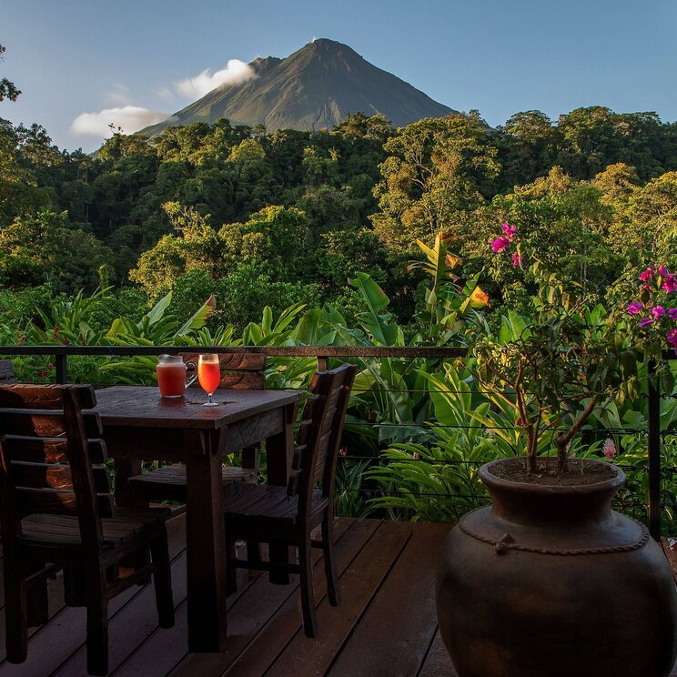 Terrasse im Hotel Amor Arenal in La Fortuna, Costa Rica, mit Blick auf den Arenal-Vulkan, umgeben von tropischer Vegetation und gemütlichem Sitzbereich.